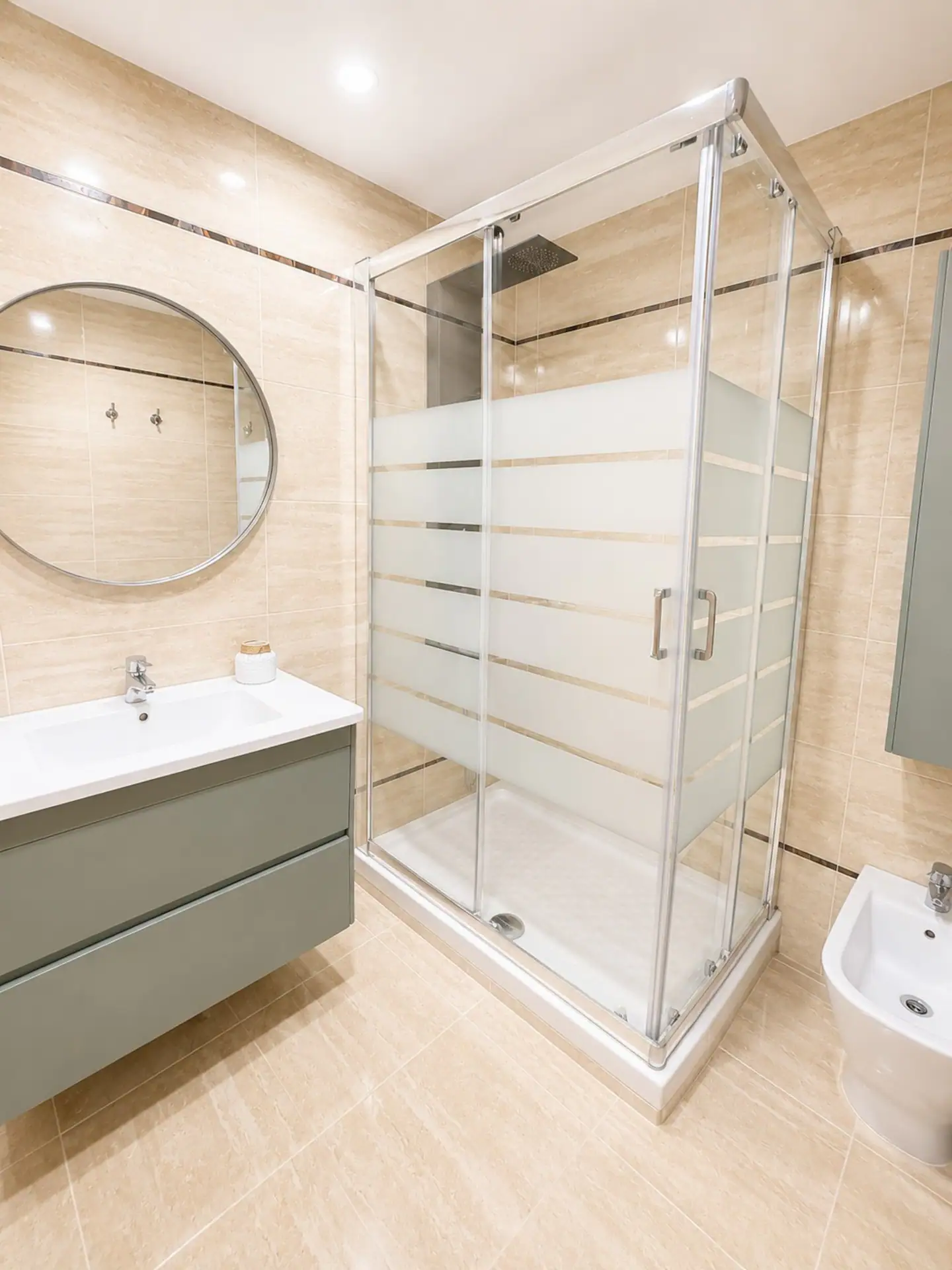 Baño con ducha de mampara, lavabo sobre mueble y espejo redondo