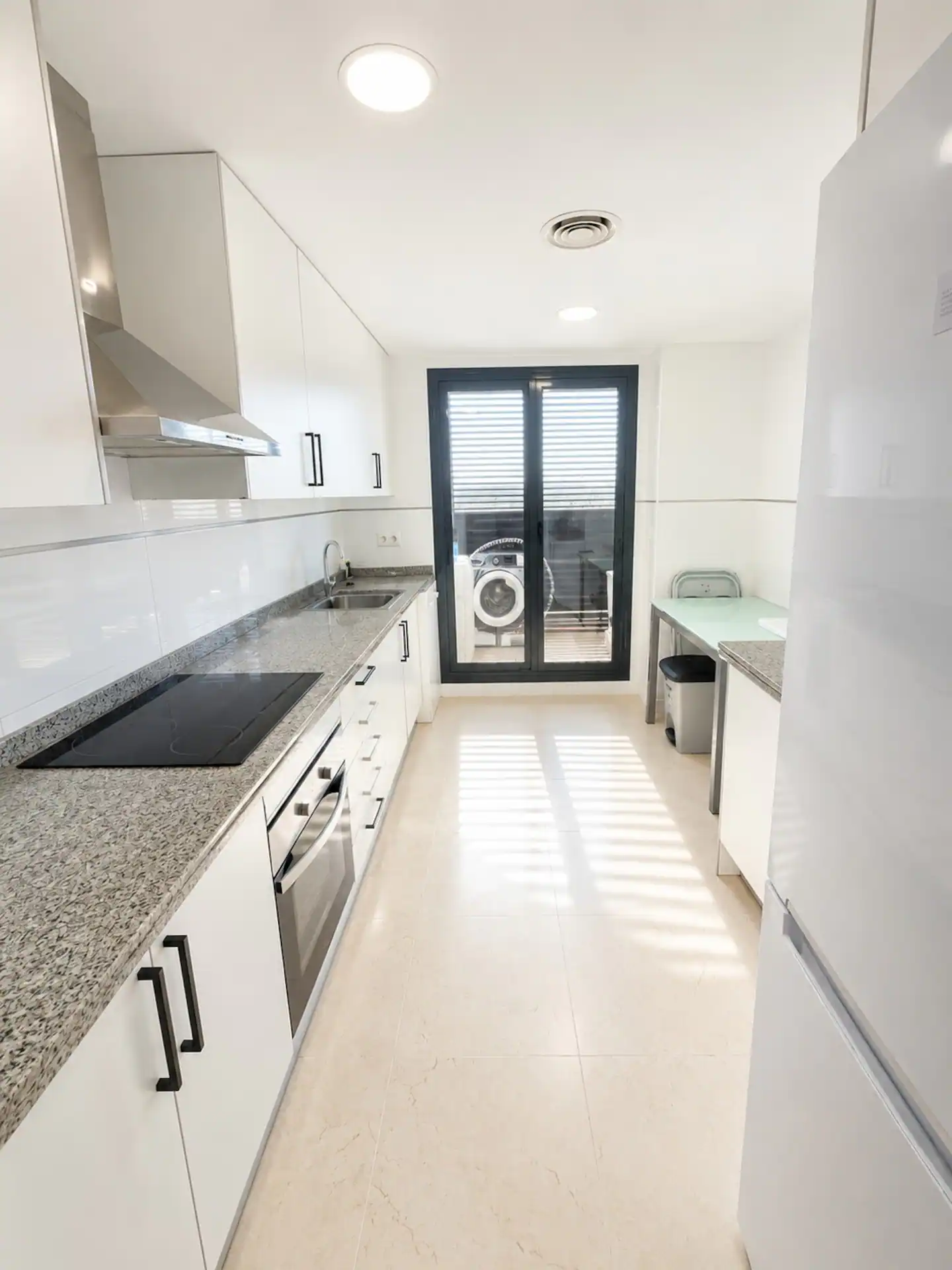 Cocina alargada en blanco con placa de inducción y horno