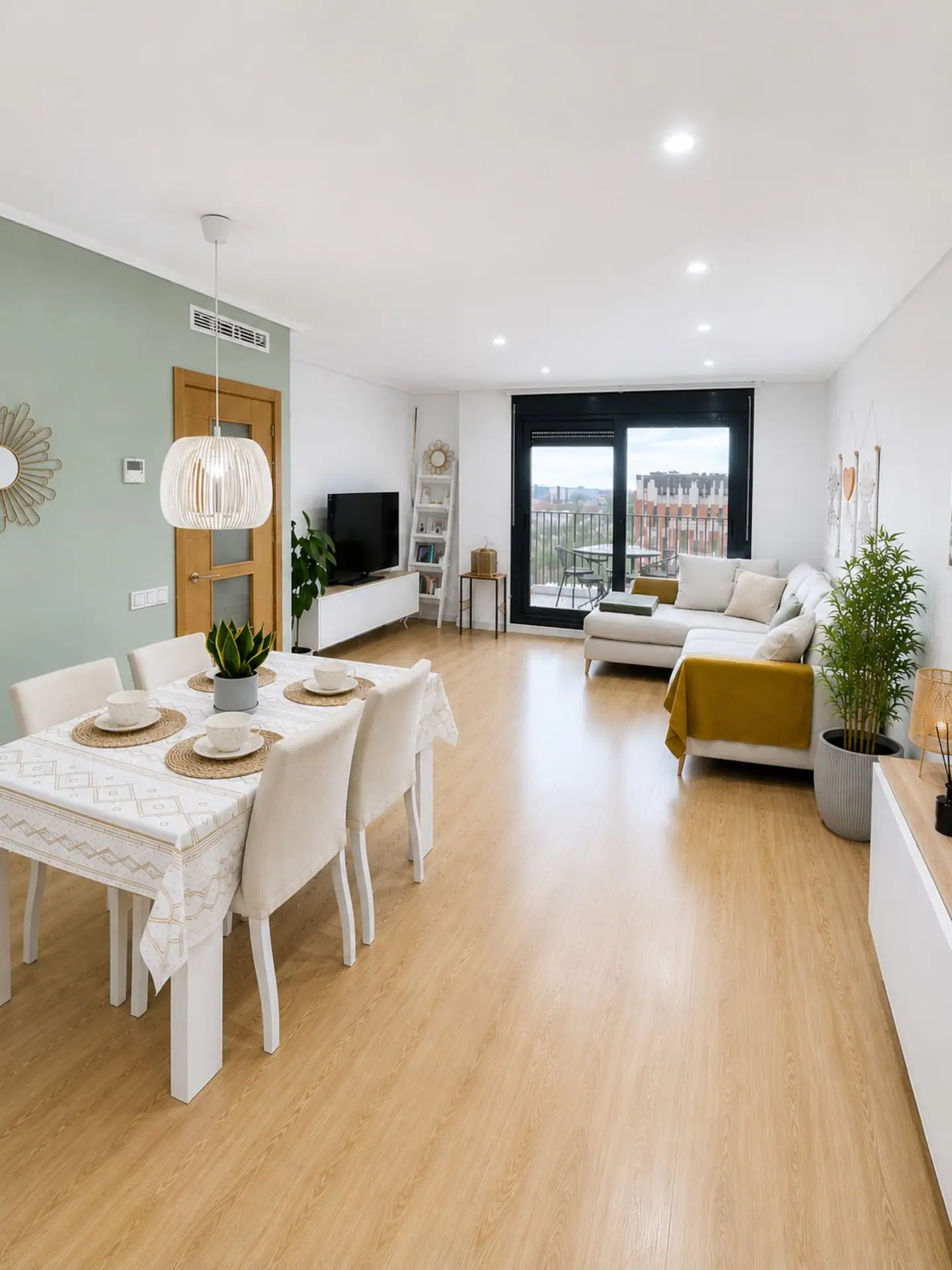 Salón comedor del apartamento de la Patacona: sofá, mesa puesta, plantas y salida al balcón
