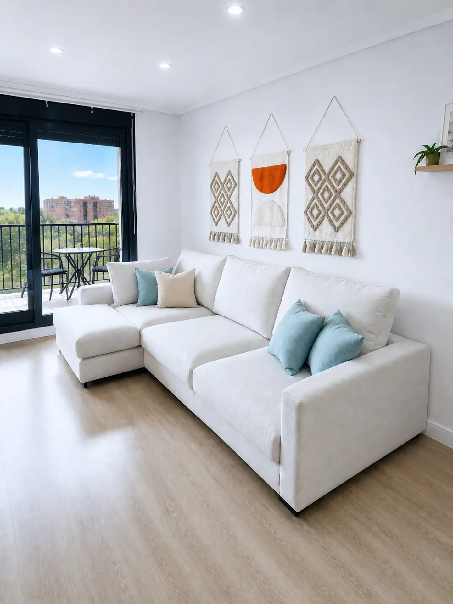 Salón con sofá chaise longue blanco, cojines turquesa y salida al balcón